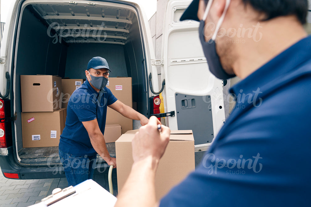 Two couriers in protective face masks unloading packages