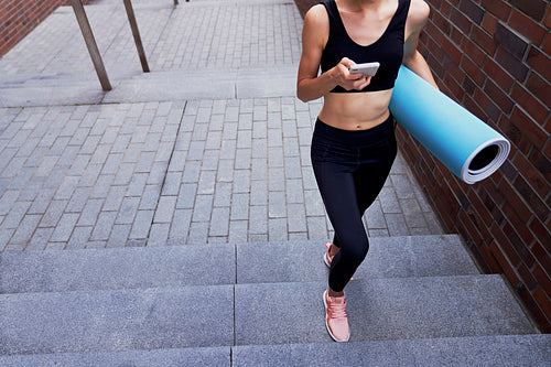 Unrecognizable woman with mobile phone and exercise mat
