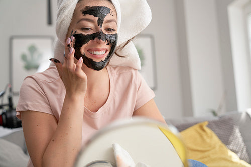 Woman applying carbon facial mask at home