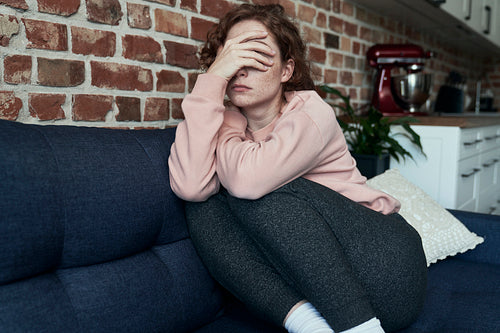 Depressed young caucasian woman sitting on sofa with eyes covered