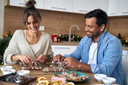 Multi ethnicity couple decorating sweet cookies at home during the Christmas