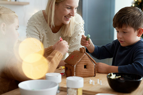 Children decorating gingerbread house with their mother