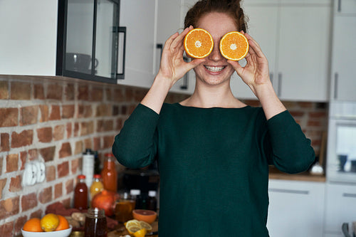 Caucasian young woman covering eyes with orange halves
