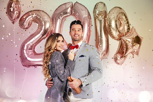 Young couple with balloons and champagne under shower of confetti