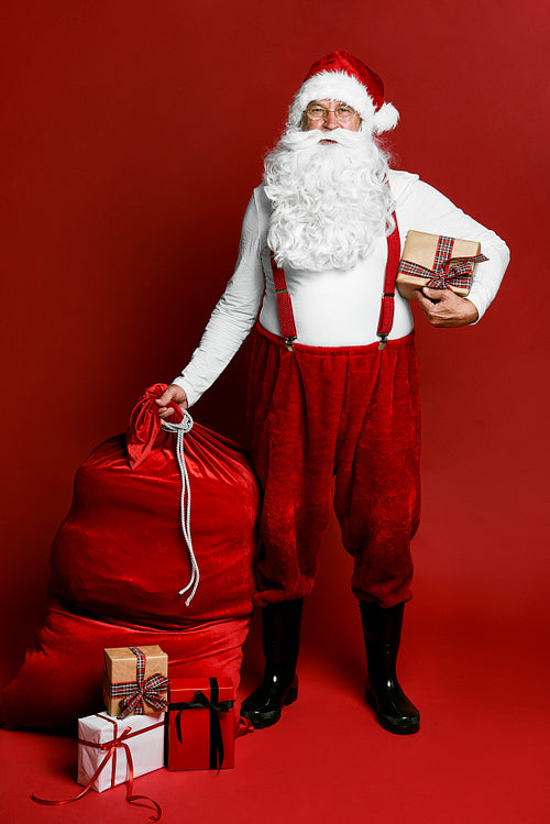 Caucasian Santa Claus standing on red background with Christmas presents