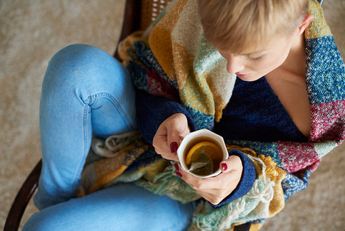 Young woman wrapped in a blanket drinking hot tea with lemon