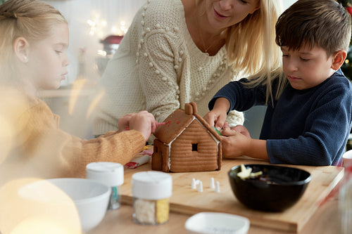 Children and mother spending time on decorating gingerbread house
