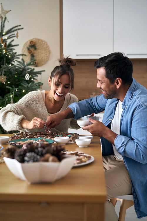 Multi ethnicity couple decorating sweet cookies at home during the Christmas