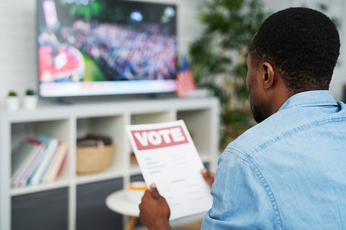 Pensive man watching tv and holding vote document