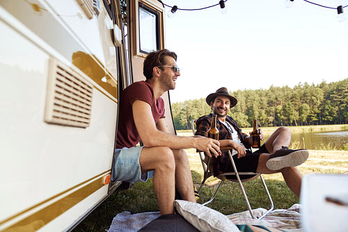 Two young male friends spending time on the camper side and drinking beer