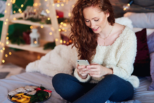 Girl with mobile phone spending christmas time in bed