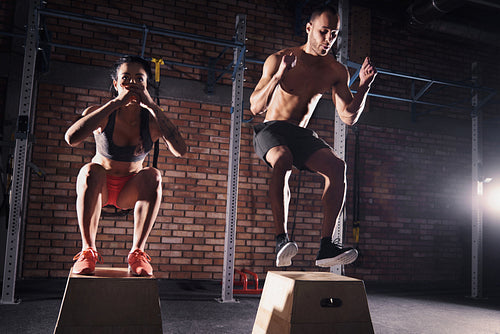 Fitness couple jumping on platforms in gym