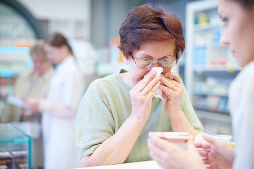 Senior woman sneezing in tissue in pharmacy