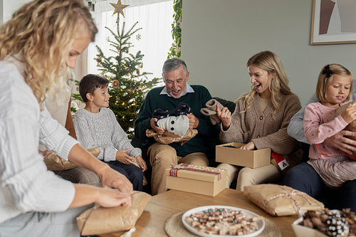 Multi generation caucasian family opening Christmas presents with ugly jumpers
