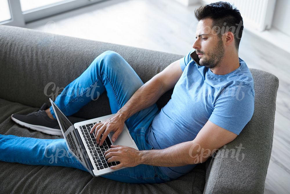 Young man using mobile phone and laptop in living room