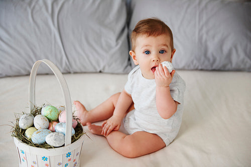 Playful baby eating easter egg on the bed