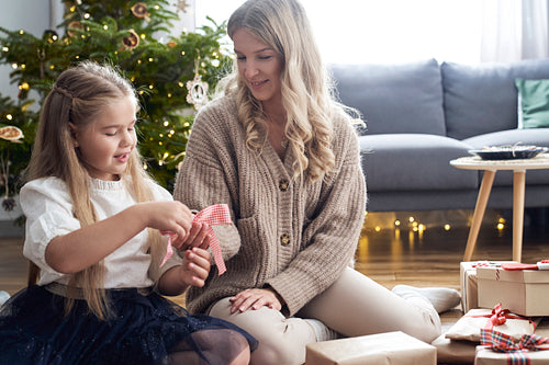 Caucasian girl and mother wrapping Christmas gifts with ribbon on the floor
