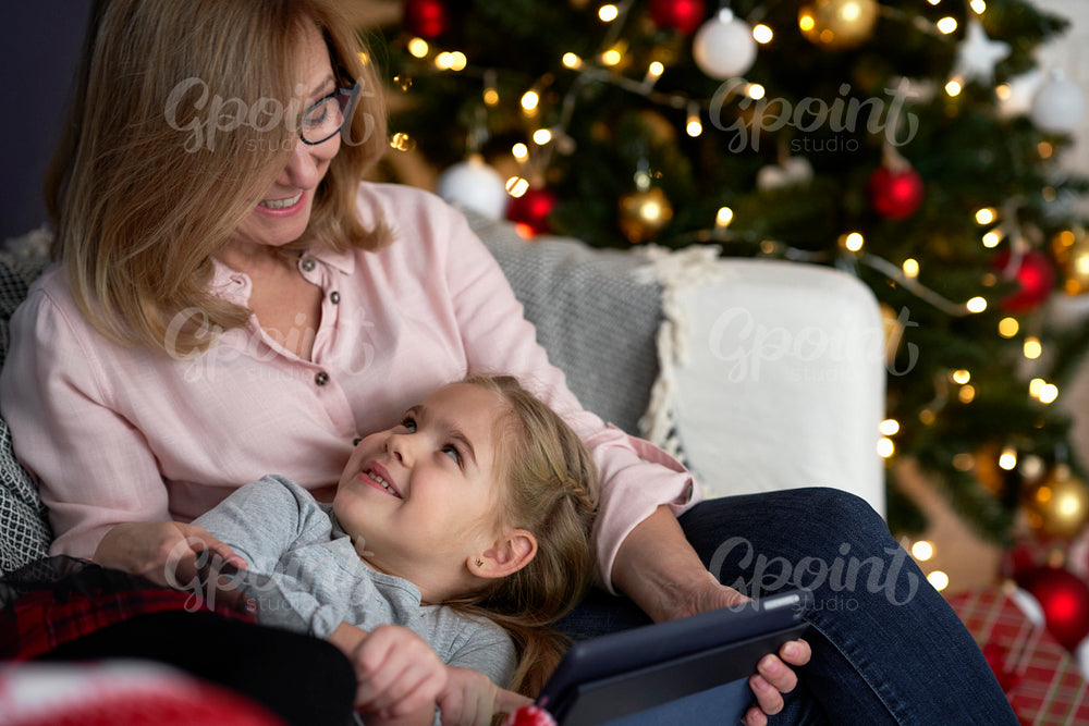 Grandmother with granddaughter using tablet while relaxing on sofa