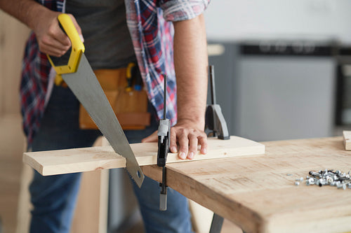 Carpenter cutting block of wood using hand saw