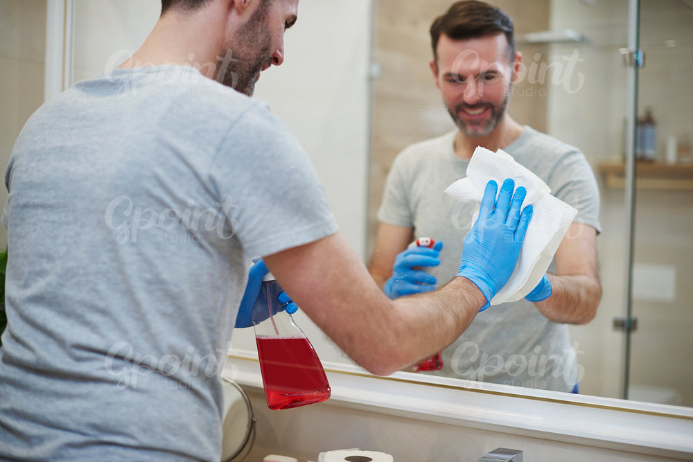 Rear view of man cleaning mirror in the bathroom