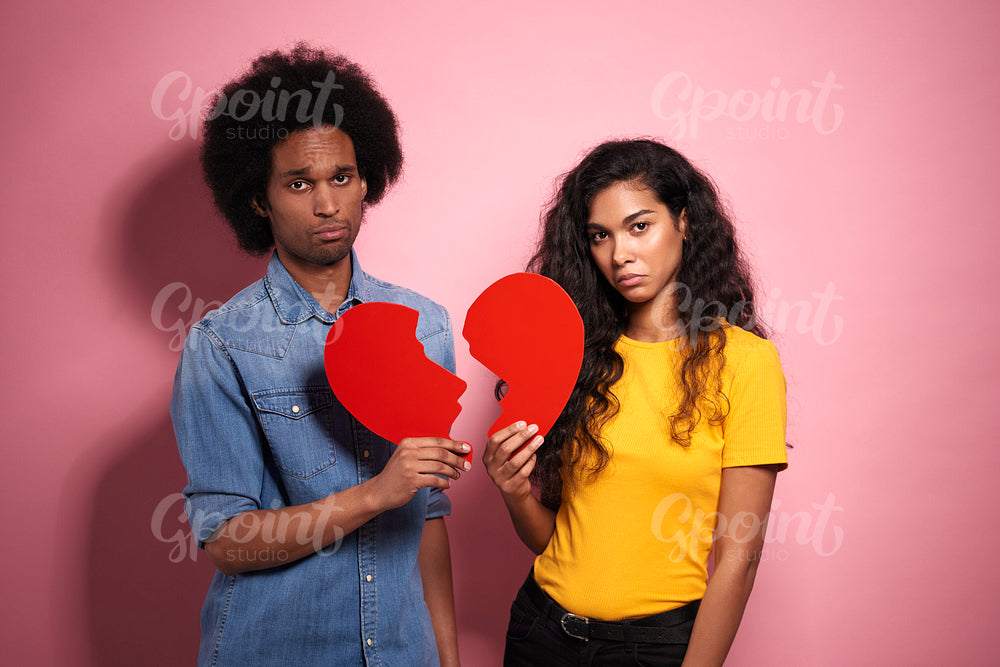 Sad African couple holding a broken heart in studio shot.