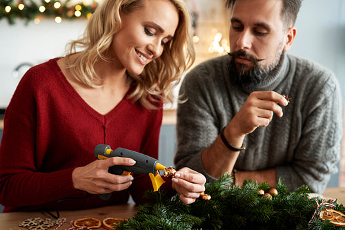Couple decorating Christmas wreaths using hot glue