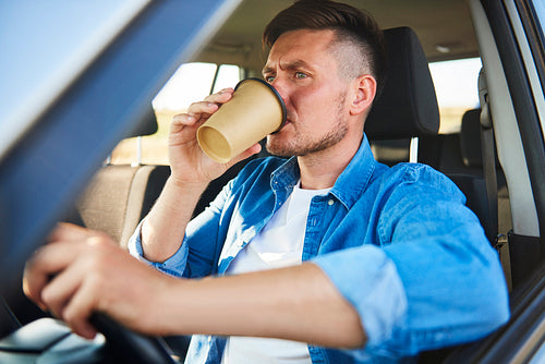 Stressed man driving a car and drinking coffee in a rush