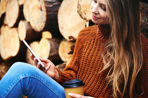 Woman relaxing with coffee cup and phone in autumnal forest