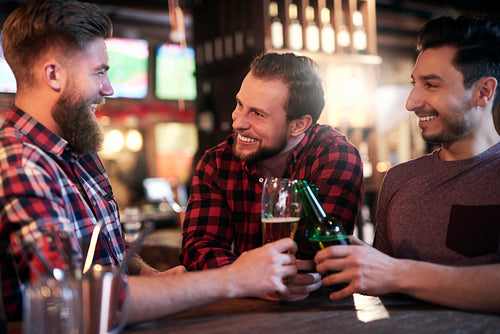 Three smiling men drinking beer in the pub