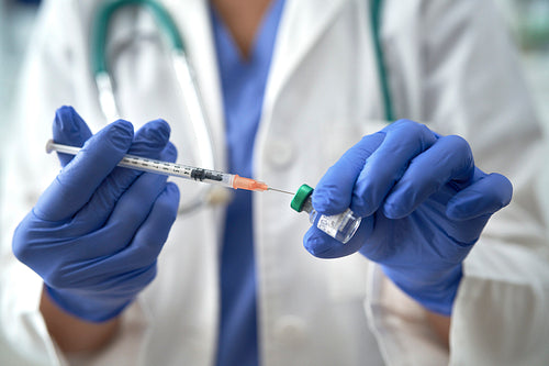 Close up of cropped hands inserting syringe into vial