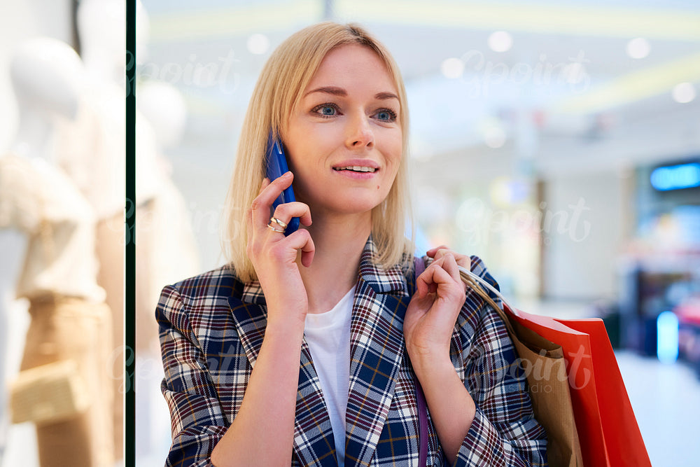 Young woman with full shopping bags talking by mobile phone