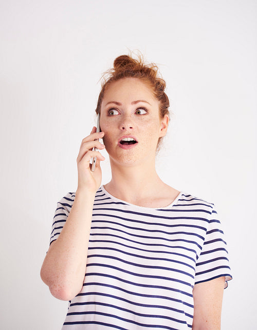 Shocked woman talking by mobile phone at studio shot
