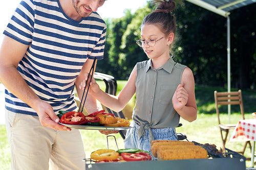 Father and daughter serving vegetables on barbecue grill
