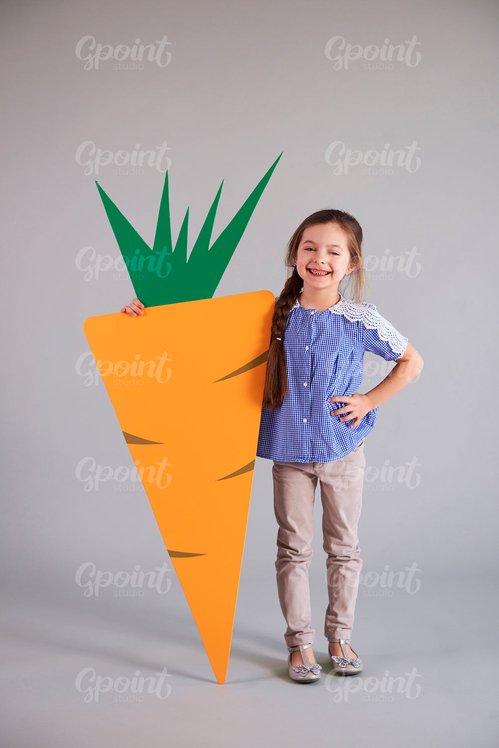 Smiling girl holding a big, artificial carrot in studio shot