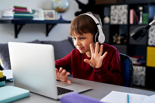 Boy using laptop and waving during video call while homework