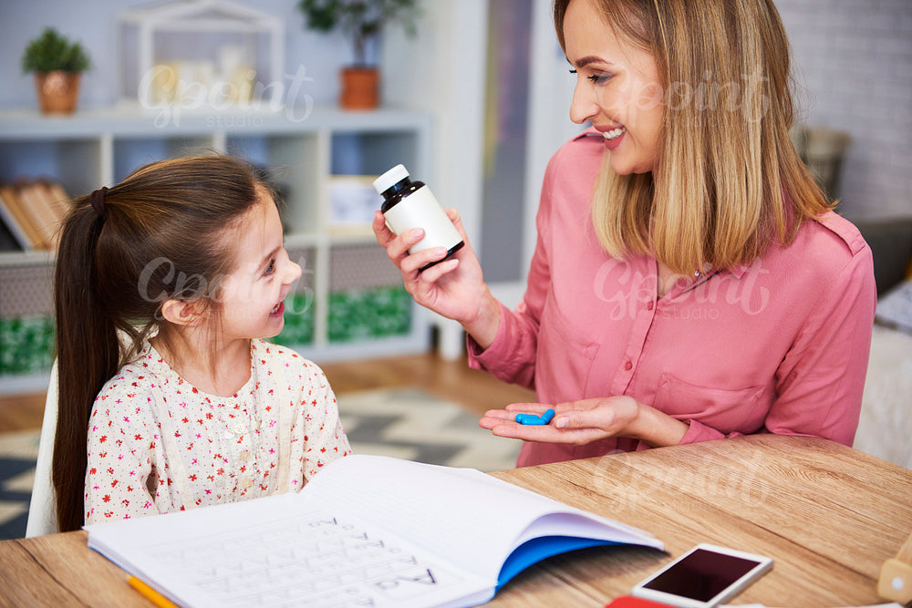 Young mother giving pills to her daughter while doing homework