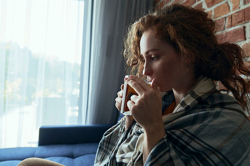 Side view of caucasian red head woman cold and drinking hot tea in the living room