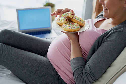 Happy pregnant woman eating donuts in bed