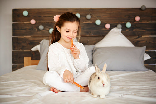 Girl and rabbit eating carrots in bedroom