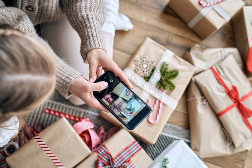 Unrecognizable woman taking picture with smart phone of wrapped Christmas presents