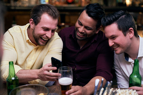 Three men using mobile phone during meeting in the pub
