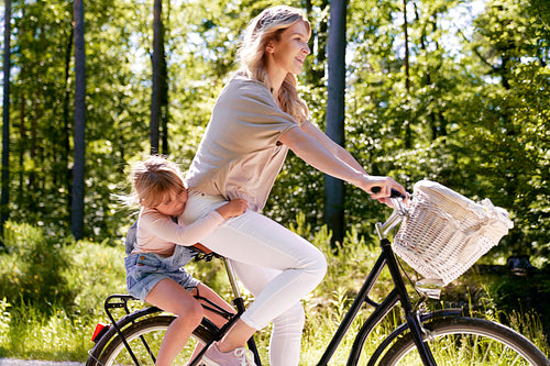 Smiling mother and daughter riding a bicycle in the forest