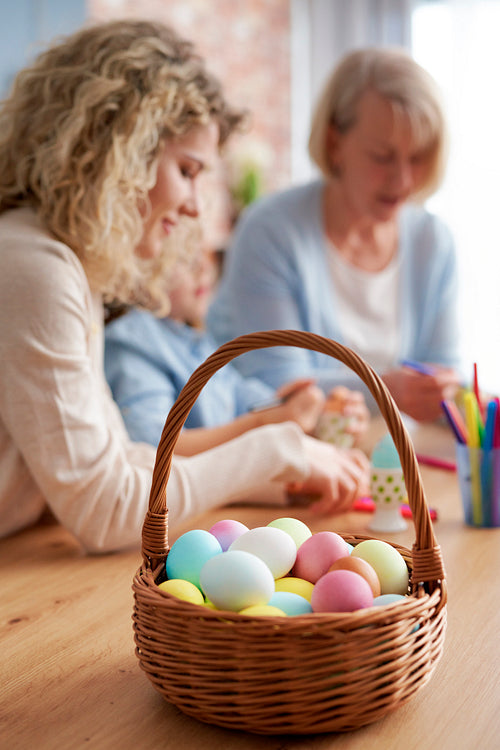 Basket full of Easter eggs and women decorate the eggs