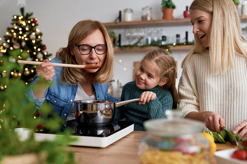 Grandma together with her daughter and granddaughter tasting Christmas dishes