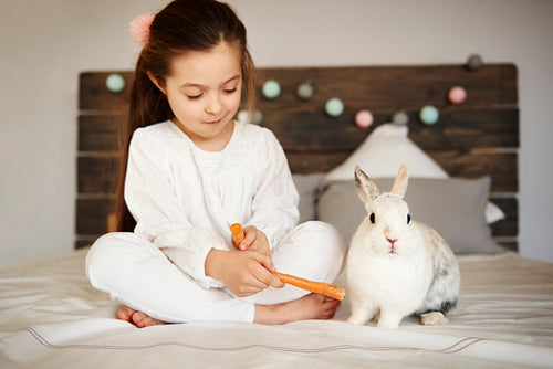 Girl feeding her rabbit on the bed