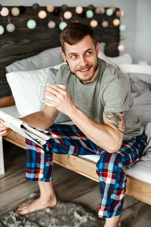 Barefoot man in pajamas with coffee sitting on bed
