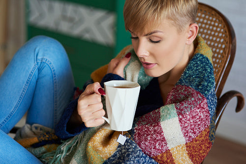 Woman wrapped in a blanket drinking tea in winter day