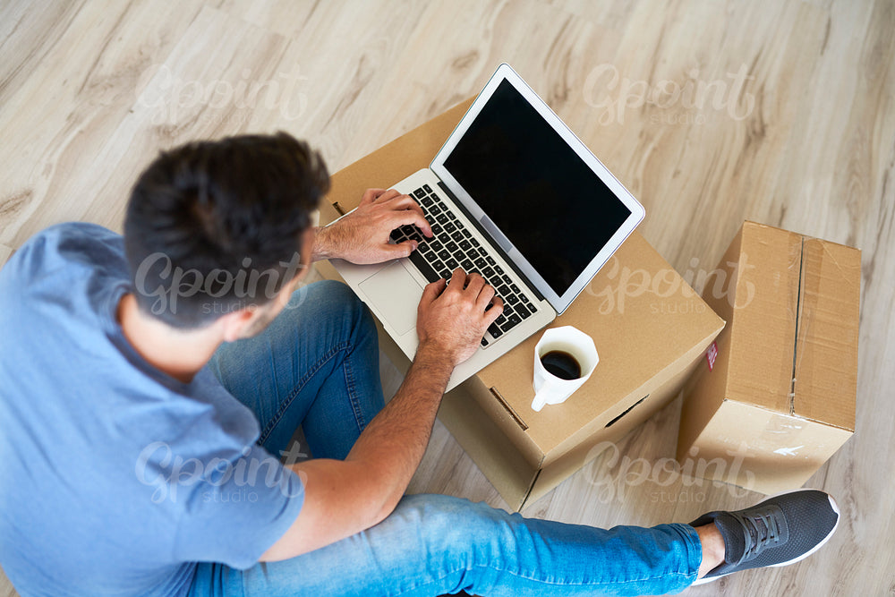 Close up of man using a laptop next to moving boxes