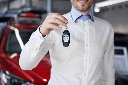 Salesman holding out car key in showroom