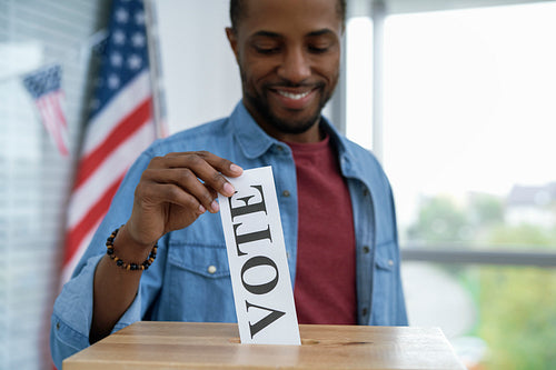Cheerful black man giving his vote into ballot box